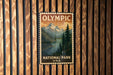 A vintage postage stamp featuring a scenic landscape with mountains, pine trees, and a lake, hanging on a wooden wall.