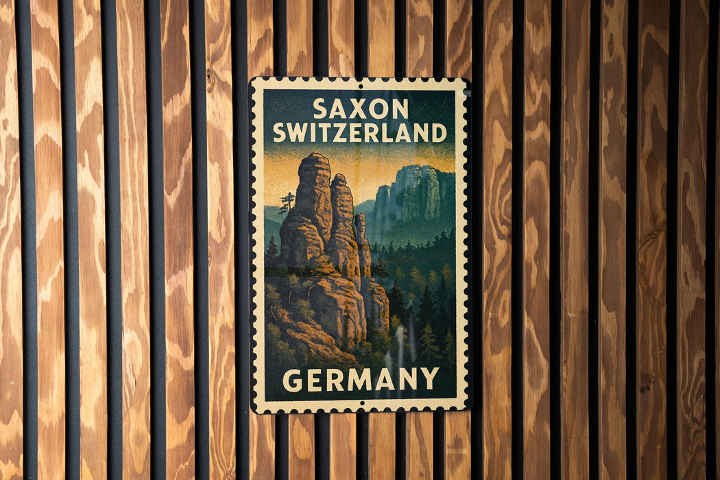 A vintage postage stamp featuring a scenic mountain landscape with the words "SAXON SWITZERLAND" and "GERMANY" printed on it, hanging on a wooden wall.