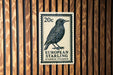A 20 cent European starling postage stamp is displayed on a wooden wall.