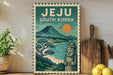 A vintage-style poster of Jeju, South Korea, featuring a mountain landscape with a sun and a stone statue, displayed on a wall next to a wooden cutting board and a potted plant.