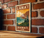 A vintage-style metal sign with the text "LÁNA'I HAWAII USA" displayed on a brick wall.