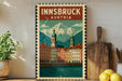 A framed poster of Innsbruck, Austria, featuring a scenic mountain landscape with colorful buildings and a river in the foreground.