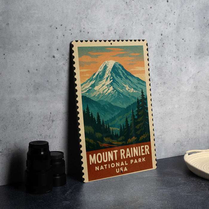 A vintage-style metal sign featuring a mountain landscape with pine trees and a snow-capped peak, with the text "MOUNT RAINIER NATIONAL PARK USA" printed on it.