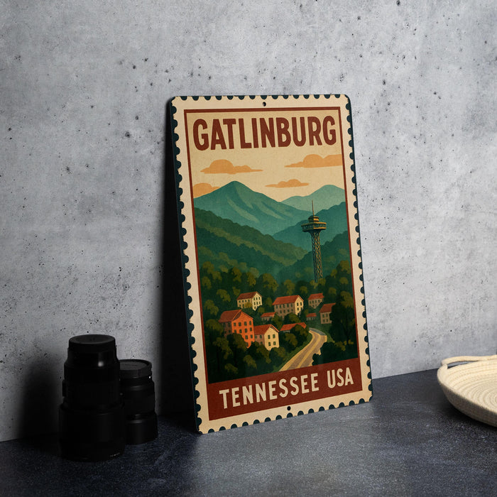 A metal sign with the text "GATLINBURG TENNESSEE USA" and an illustration of a mountain town with a tower, placed on a gray countertop next to some black camera lenses.