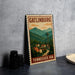 A metal sign with the text "GATLINBURG TENNESSEE USA" and an illustration of a mountain town with a tower, placed on a gray countertop next to some black camera lenses.