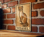 A sign featuring a weasel illustration is mounted on a brick wall.