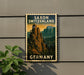 A vintage postage stamp depicting Saxon Switzerland, featuring a mountain landscape with trees and a castle, is displayed on a wall.