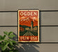 A vintage-style metal sign with the text "OGDEN" and "UTAH USA" displayed on it, featuring an illustration of a mountain landscape with a clock tower.