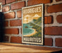 A vintage-style stamp or sign with the text "RODRIGUE" and "Mauritius" printed on it, hanging on a brick wall.