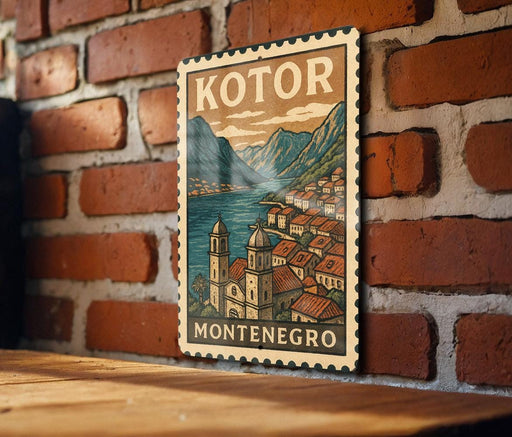A vintage-style postage stamp depicting a scenic view of the town of Kotor, Montenegro, with mountains and buildings in the background.