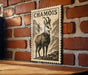 a wooden table with a framed print of a chamois, a mountain goat, mounted on a brick wall.