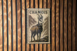 a metal stamp with a depiction of a mountain goat, mounted on a wooden wall.