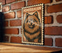 A framed illustration of a pomeranian dog is displayed on a brick wall.