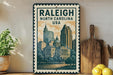 A framed poster of the Raleigh, North Carolina skyline, featuring a cityscape with tall buildings and a dome, is displayed on a shelf next to a wooden cutting board and some lemons.