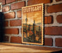 A vintage-style poster of Stuttgart, Germany, featuring a cityscape with a tower and other architectural elements, is displayed on a brick wall.