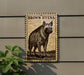 a wooden sign with a hyena illustration, mounted on a wall next to a plant.