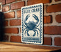 A metal sign with a blue crab illustration is mounted on a brick wall.