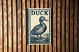 A metal sign with the word "DUCK" on it is mounted on a wooden wall.