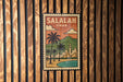 A vintage-style poster of Salalah, Oman, featuring a palm tree and a cityscape, is displayed on a wooden wall.