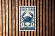 A blue crab sign is displayed on a wooden wall.