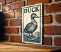 A sign featuring a duck is mounted on a brick wall.