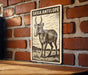 a sign with a picture of a goat, mounted on a brick wall.