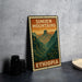 A vintage-style metal sign with the text "SIMIEN MOUNTAINS ETHIOPIA" printed on it, depicting a mountainous landscape. The sign is placed on a gray countertop next to some black camera lenses.