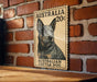 a wooden surface with a framed illustration of a black and tan Australian Cattle Dog on a brick wall.