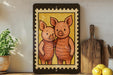 a framed illustration of two cartoon pigs standing close together, with a wooden cutting board and a potted plant visible in the background.