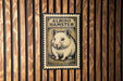 A metal sign with a hamster illustration is mounted on a wooden wall.