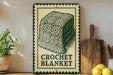 A vintage-style sign for a crocheted blanket is displayed on a wooden shelf, accompanied by a potted plant, a wooden cutting board, and some lemons.