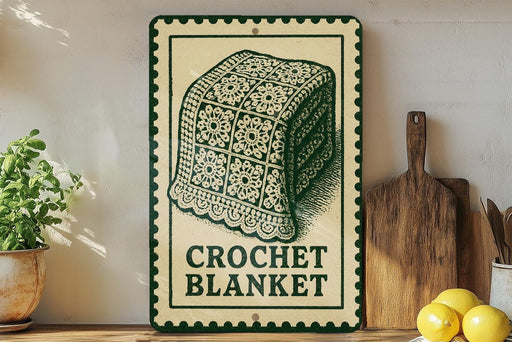 A vintage-style sign for a crocheted blanket is displayed on a wooden shelf, accompanied by a potted plant, a wooden cutting board, and some lemons.