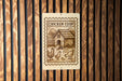 A sign with a wooden background and a stamp-like design, featuring a house and chickens, mounted on a wooden wall.