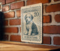 A metal sign featuring a dog illustration and the text "SHEEPADOLE 20 MINIATURE" is mounted on a brick wall.