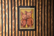 A framed illustration of two cartoon pigs embracing each other is displayed on a wooden wall.