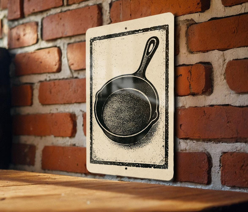 A sign featuring a black and white illustration of a frying pan is mounted on a brick wall.