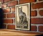 A metal sign featuring a black and white illustration of a cat, mounted on a brick wall.