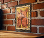 A framed illustration of two cartoon pigs is hanging on a brick wall.