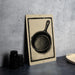 a black and white illustration of a frying pan on a wall, accompanied by a stack of black containers and a woven basket.
