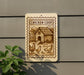 a sign with a picture of a chicken coop and chickens, mounted on a wall next to a plant.