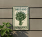 a sign for "Oregano Bunch" hanging on a wall, with a plant to the left of the sign.
