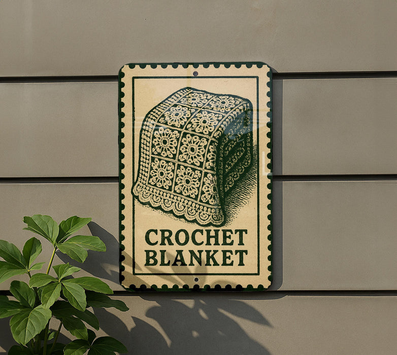 a sign that reads "Crochet Blanket" with a decorative border, mounted on a wall next to a plant.