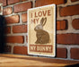 A sign with the text "I LOVE MY BUNNY" and an illustration of a rabbit is displayed on a brick wall.