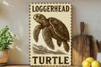 A wooden sign with a turtle illustration and the word "Loggerhead" written on it, placed on a wooden surface next to a potted plant and a cutting board.