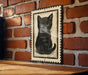 A black and white illustration of a cat is displayed on a brick wall, mounted on a wooden surface.