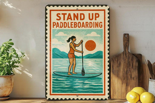A vintage-style metal sign with a woman paddleboarding on a blue surfboard, surrounded by kitchen utensils and a potted plant.