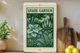 A framed image of a lush green garden with white flowers, placed on a shelf next to a wooden cutting board and a potted plant.
