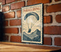 A vintage-style poster of a person paragliding is displayed on a brick wall, with a wooden table below it.