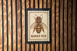A honey bee illustration on a wooden surface, with the text "HONEY BEE" below it.