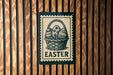 A sign with the word "EASTER" on it, featuring a basket of Easter eggs, is displayed on a wooden wall.